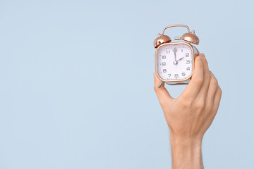 Male hand holding alarm clock on blue background