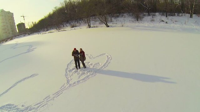 Couple stands inside heart painted on snowbound pond near houses