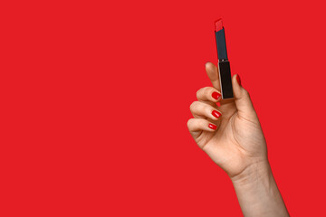 Female hand with red manicure holding lipstick on color background
