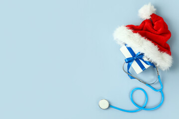 Santa hat with stethoscope and Christmas gift on color background