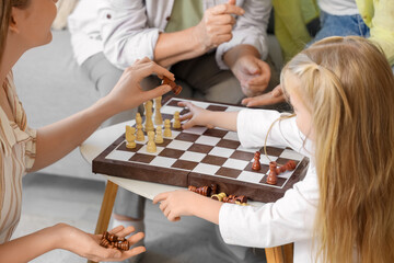 Little girl with her family playing chess at home, closeup