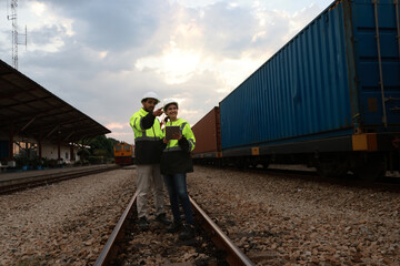 Two engineers with green safety jackets work checking cargo at the train station 