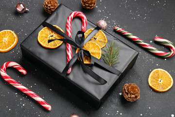 Christmas gift box with dried orange slices, candy canes and pine cones on black background