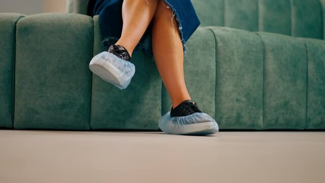 Close-up shot of the legs in shoe covers of a young girl sitting in the lobby of a medical center before an appointment with doctor