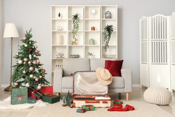 Suitcase with clothes, gift boxes and beautiful Christmas tree in light living room