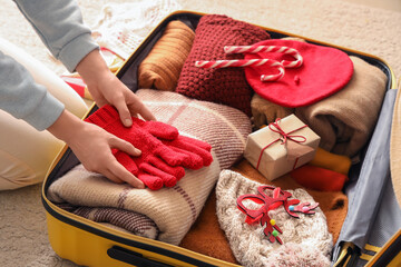Woman packing clothes, Christmas gift and decor into suitcase, closeup