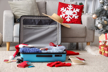Suitcase with clothes, beach accessories, credit cards and Christmas decor on floor in room - obrazy, fototapety, plakaty