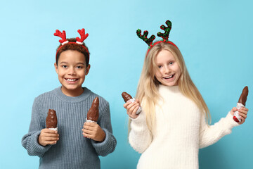 Cute little children in reindeer horns with chocolate Santa Claus on blue background