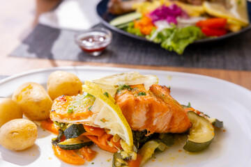 Grilled salmon with potatoes and vegetables on a white plate in a restaurant