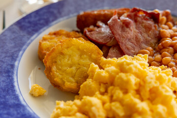 English breakfast with crispy hash brown patties, bacon, scrambled eggs baked beans on a plate. Selective focus. 