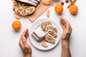 Male hands with tasty Christmas stollen and tangerines on white background