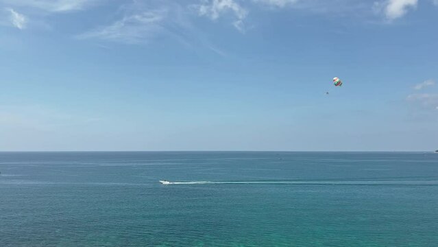 The coast of Thailand on a sunny day, beach entertainment - parachute behind a motorboat, people parachute over the sea