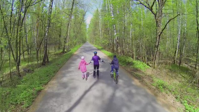 Three people ride on rollerskates and bike by road 