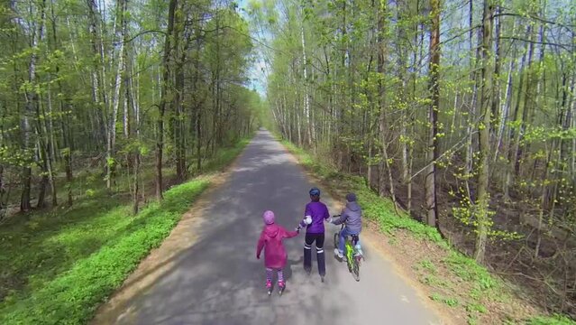mother with kids ride on rollerskates and bike by road