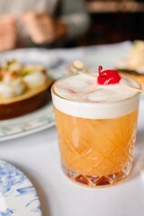 An amaretto sour cocktail topped with maraschino cherry at a French bistro-style restaurant in Circular Quay, Sydney (a plate of escargot in the background) — New South Wales, Australia