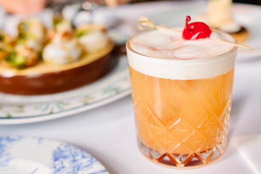 An amaretto sour cocktail topped with maraschino cherry at a French bistro-style restaurant in Circular Quay, Sydney (a plate of escargot in the background) — New South Wales, Australia
