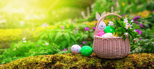 Basket with Easter eggs with handmade funny rabbit a trunk of a mossy tree in the spring forest,...