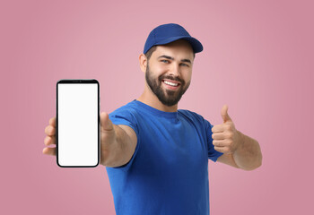 Happy courier holding smartphone with empty screen and showing thumbs up on pink background