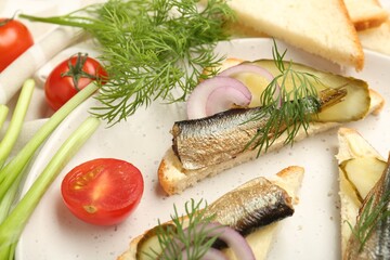 Delicious sandwiches with sprats, pickled cucumber, onion and dill served on plate, closeup