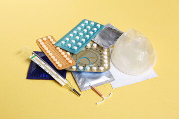 Contraceptive pills, condoms, intrauterine device and thermometer on yellow background. Different...