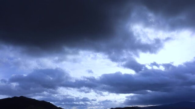 Stormy sky timelapse: Time-lapse video of a lightning bolt amid dark, evocative storm clouds gathering over a mountainous landscape during a twilight evening with a melancholic atmosphere