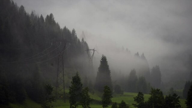 Misty mountain landscape with dense evergreen forest and power lines in the moody atmosphere. A summer storm in the forest with rain and fog at low altitude in Val di Fassa, Moena, Trento, Italy