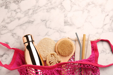 Net bag with different items on white marble table, top view and space for text. Conscious...