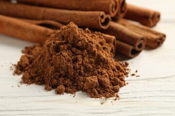 Aromatic cinnamon powder and sticks on white wooden table, closeup