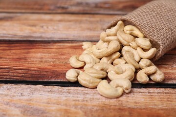 Sack with tasty cashew nuts on wooden table, closeup. Space for text