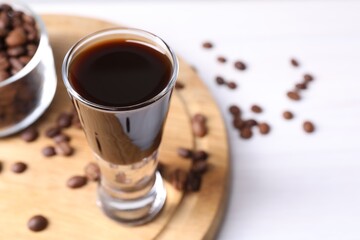 Shot glass of coffee liqueur and beans on white table, closeup. Space for text