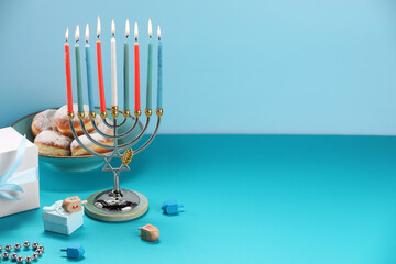 Hanukkah celebration. Menorah with burning candles, dreidels, donuts and gift boxes on table...