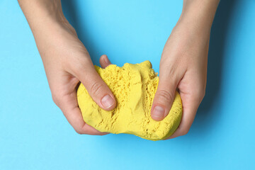 Woman playing with yellow kinetic sand on light blue background, top view