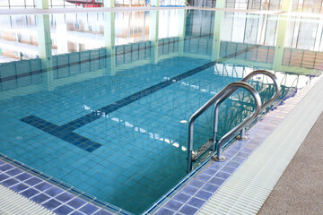 Metal stairs in the pool. Shiny stainless steel railing next to a swimming pool in a building with...