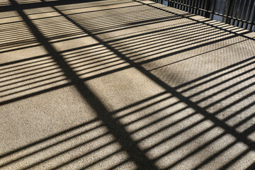 Light and shadow on the steel frame on the floor. Shadows of sunlight shining through metal frames on rough brown cement floor with selective focus.