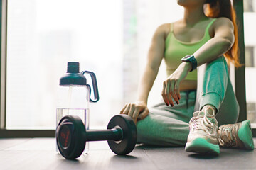 Good looking - beautiful Asian woman relaxing in the gym after made weight training and cardio workout, woman sitting or resting on the bench while drinking water after exercise.