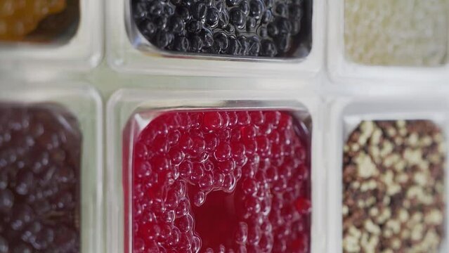 Bobas of different flavors for the preparation of bubble tea drink on display. Slow motion, vertical video.