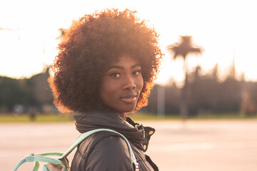 beautiful black woman with afro hair looking and smiling with sunset view on a sunny day in the...