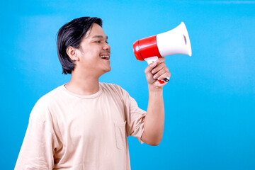 Cheerful Asian male with megaphone making loud marketing advertisement on light blue background