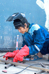 Asian worker wearing protective gloves and mask measuring metal rod at house renovation site