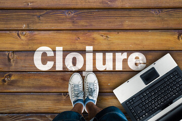 Legs in sneakers standing next to laptop and Clojure on wooden floor. Clojure programming language.
