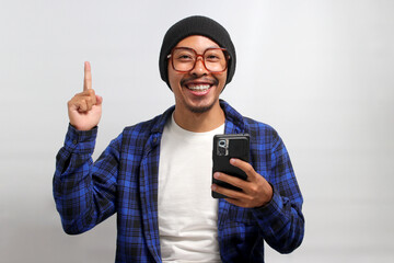 Asian man wearing beanie hat, casual shirt, and eyeglasses points at an empty space while...