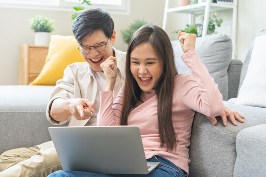 Happy excited, smiling asian young couple love using laptop computer, great deal or business success, received or getting cash back, tax refund, good news by mail while sitting in living room at home.
