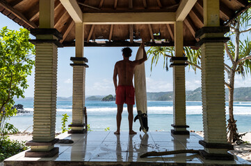 Surfer contemplating the waves from beachside pavilion, Indonesia, Asia
