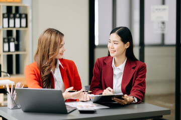 Two Asian businesswoman discuss investment project working and planning strategy with tablet laptop computer in office.