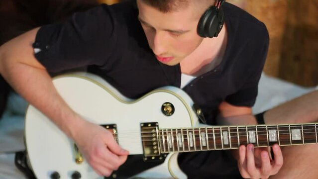 Young man in headphones yank strings of electric guitar