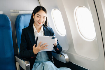 Asian executive excels in first class, multitasking with digital tablet, laptop. Travel in style, work with grace..