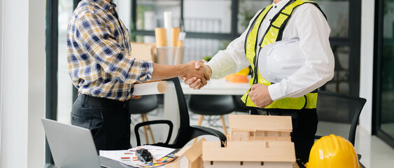 Construction team shake hands greeting start new project plan behind yellow helmet on desk in office