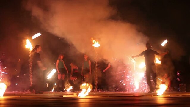 Boys move synchronously rotating burning pois at fire show.