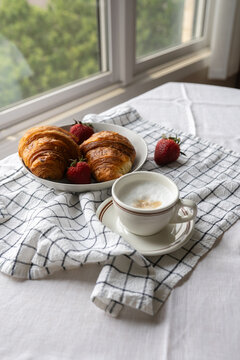 French croissants in a woven basket, complemented by a cup of coffee with milk. A delightful breakfast moment, a blend of pastry perfection.