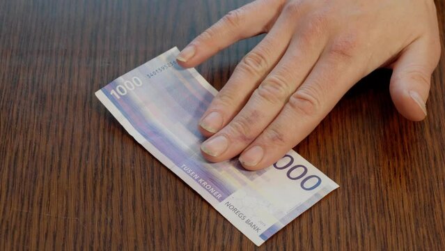 Hand Placing Norwegian 1000 kr Note in center of Wooden Table